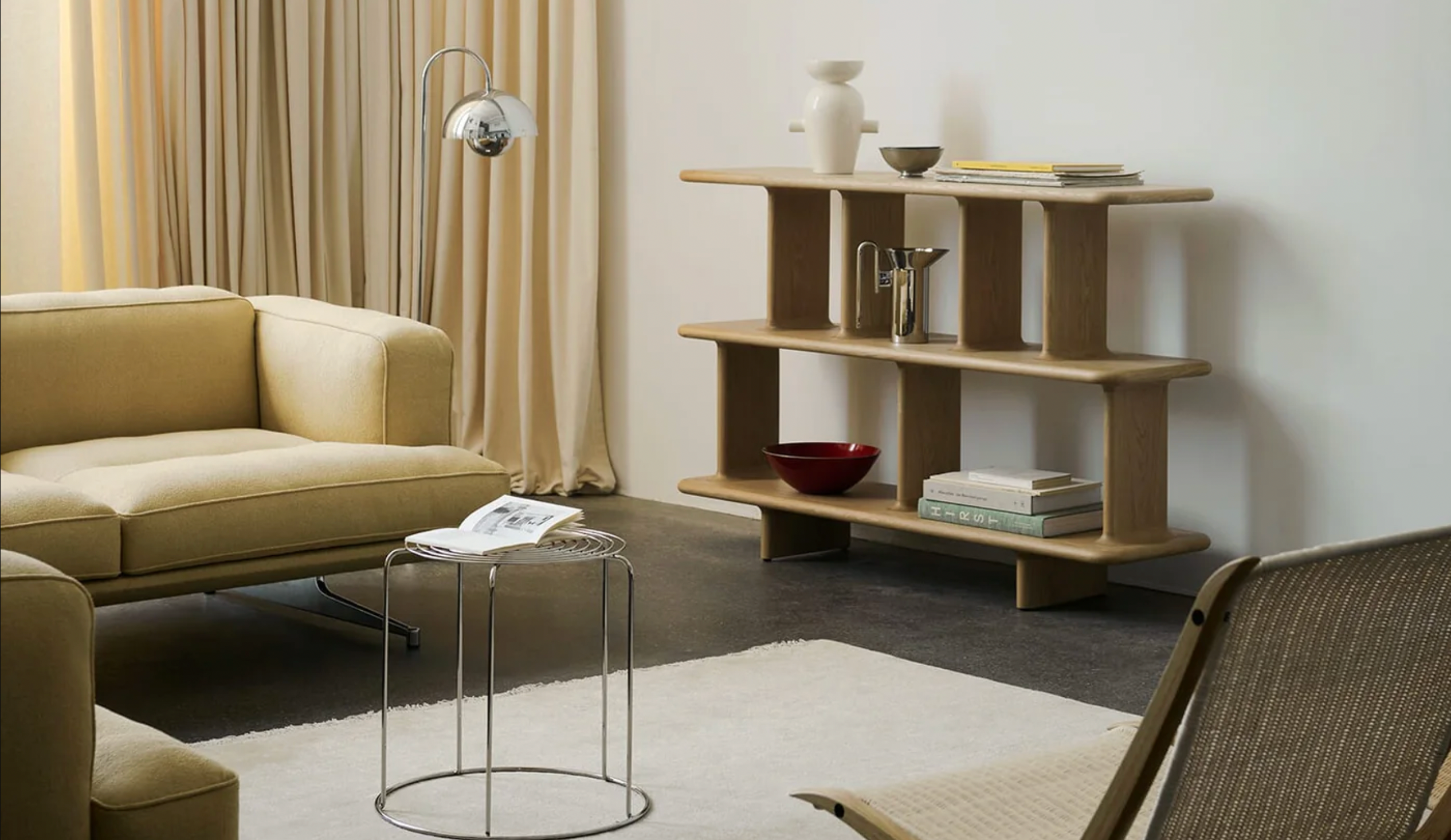 Et lyst, moderne stueområde med beige sofa, trehylle med dekor, glassbord og myke tekstiler i en rolig, skandinavisk stil.