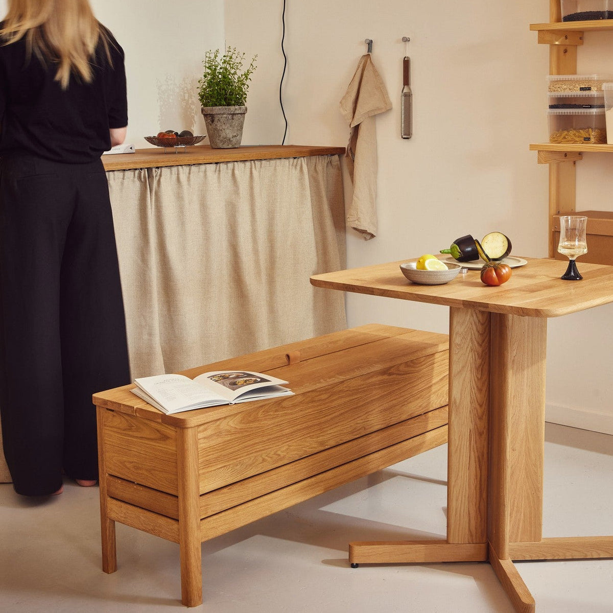 Minimalistisk spiseplass med trestol, eikebord og hylle i lyst treverk, dekorert med keramikk og oppbevaringsbokser i et nordisk interiør.
