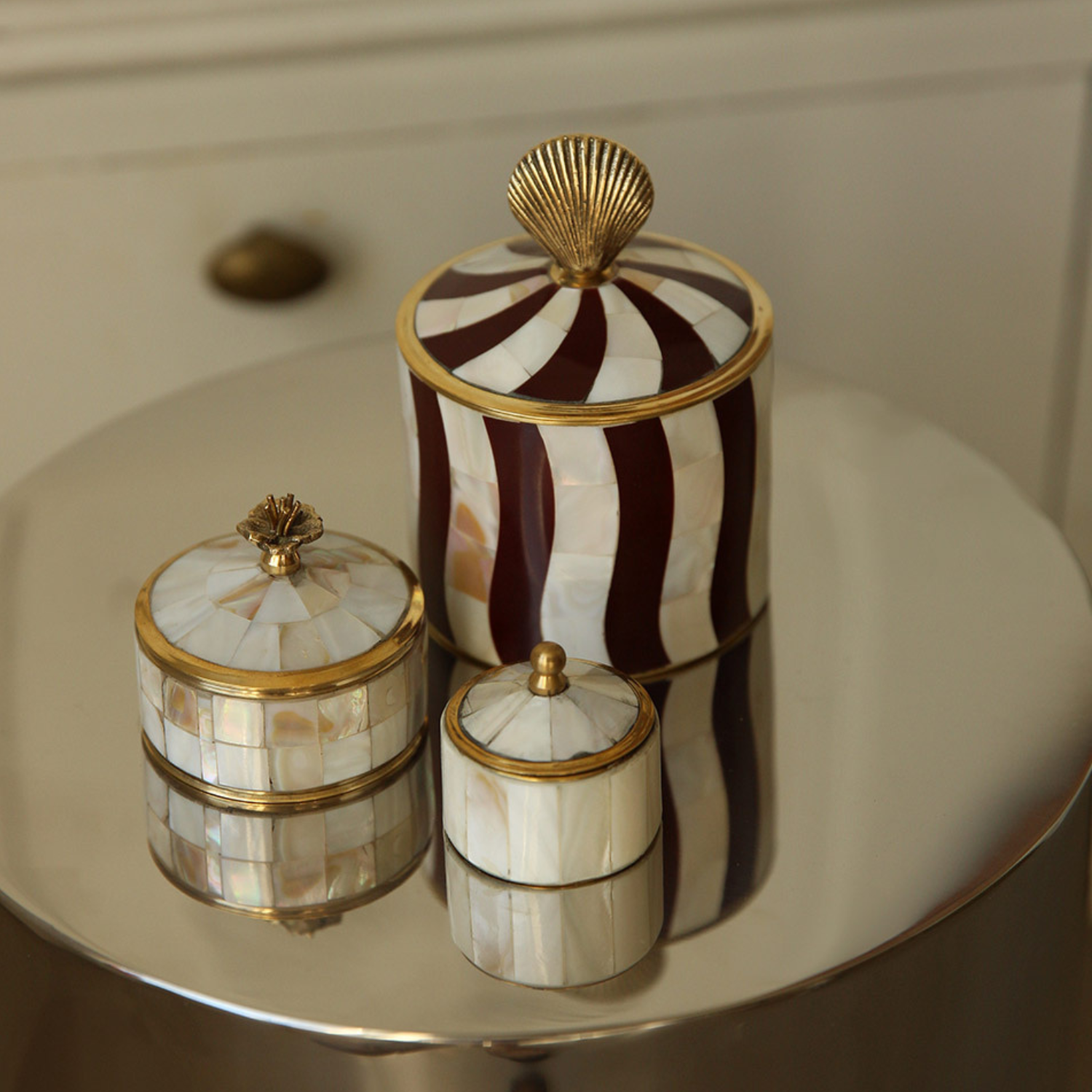 Dekorative bokser i perlemor og messing på et blankt bord, i varme toner med elegant og tidløst uttrykk.