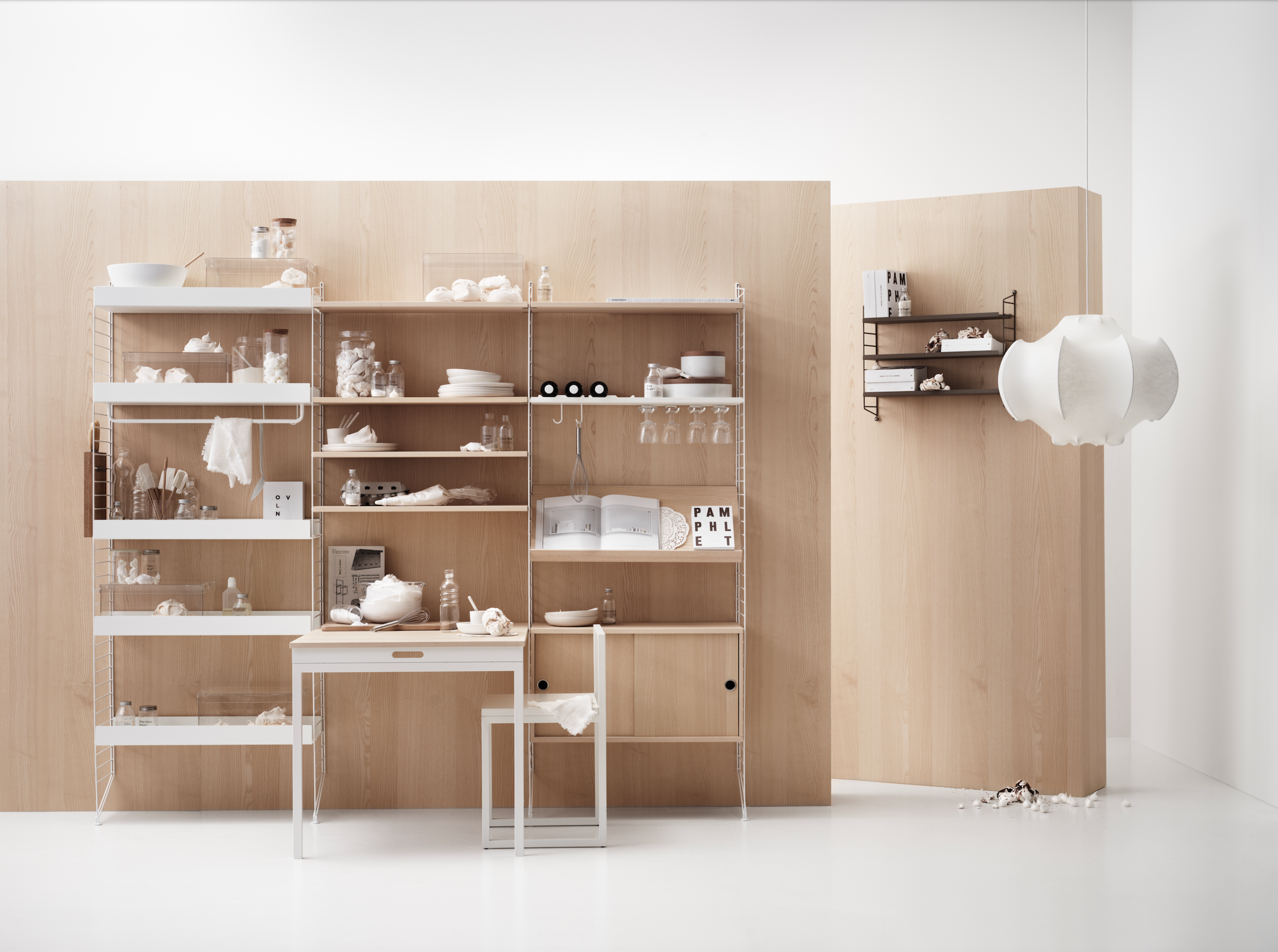 Lyst interiør med modulbasert hyllesystem i lyst tre og hvitt metall, fylt med glass, servise og kjøkkenutstyr – stilrent oppsett som viser fleksibel oppbevaring og nordisk design.