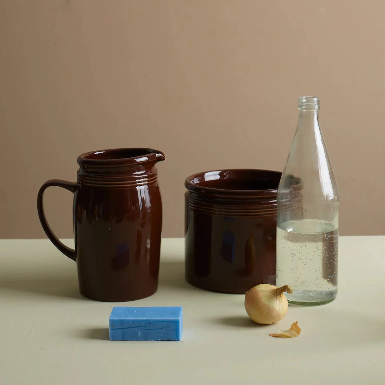 Et stilrent oppsett med elegante glass og en lys, skulpturell vinkjøler formet som en skjellform. En champagneflaske står kjølt i midten, omgitt av serveringsglass og en moderne karaffel på et brunt lintøy som skaper en varm, luksuriøs stemning.