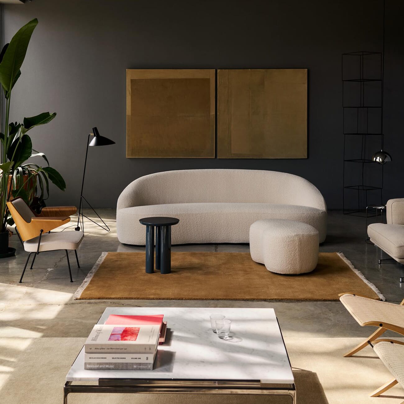 En moderne stue med en myk, kremfarget sofa og matchende puff. Rommet er stylet med varme jordtoner, et stort teppe, minimalistiske møbler og kunst på veggen. Naturlig lys faller inn og skaper en rolig, elegant atmosfære.