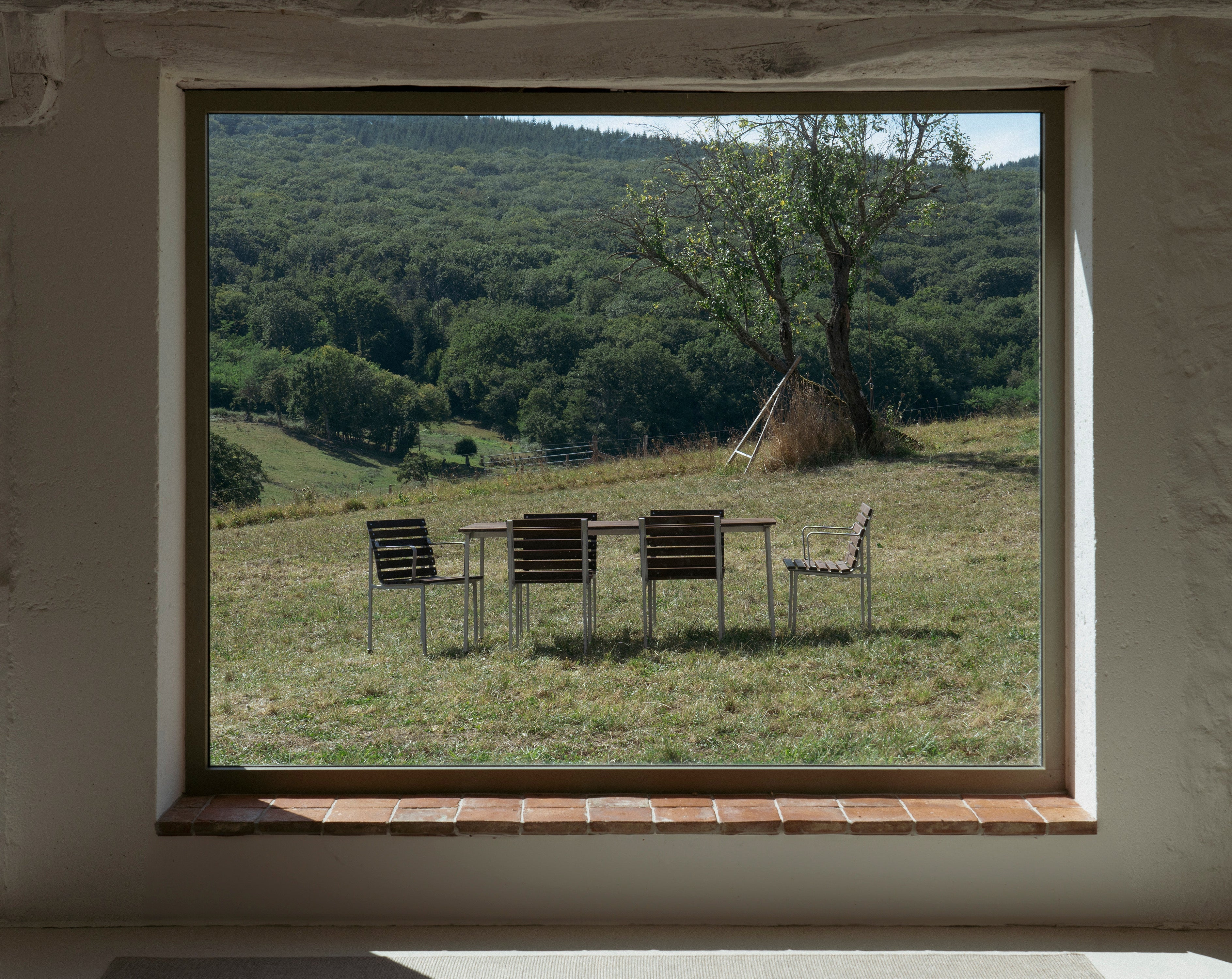 Lyst spiseområde med rund spisebord og polstrede stoler i duse toner, dekorert med vase, bøker og moderne interiør ved store vinduer.
