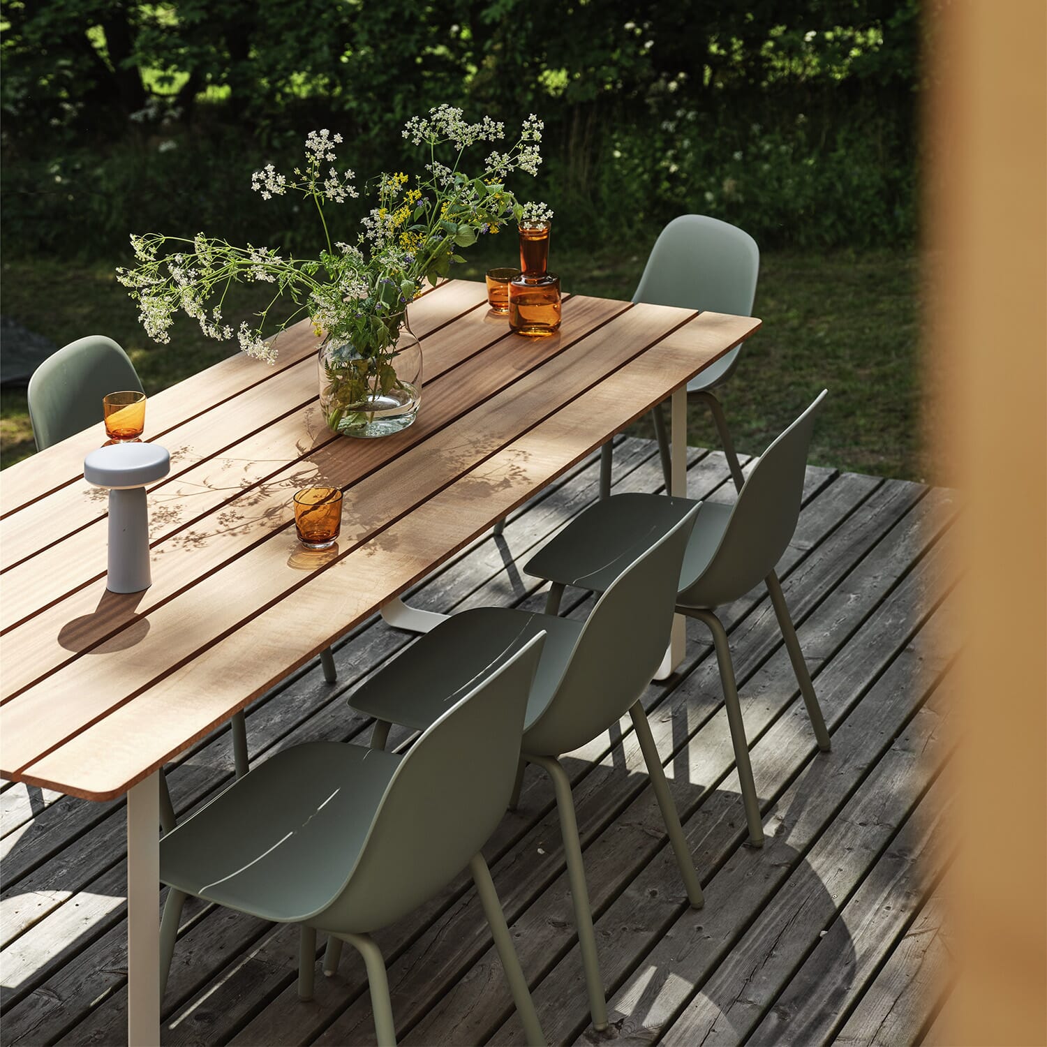 Spisebord til utebruk i tre på terrasse med grønne utestoler, dekorert med vase og glass i sommersol