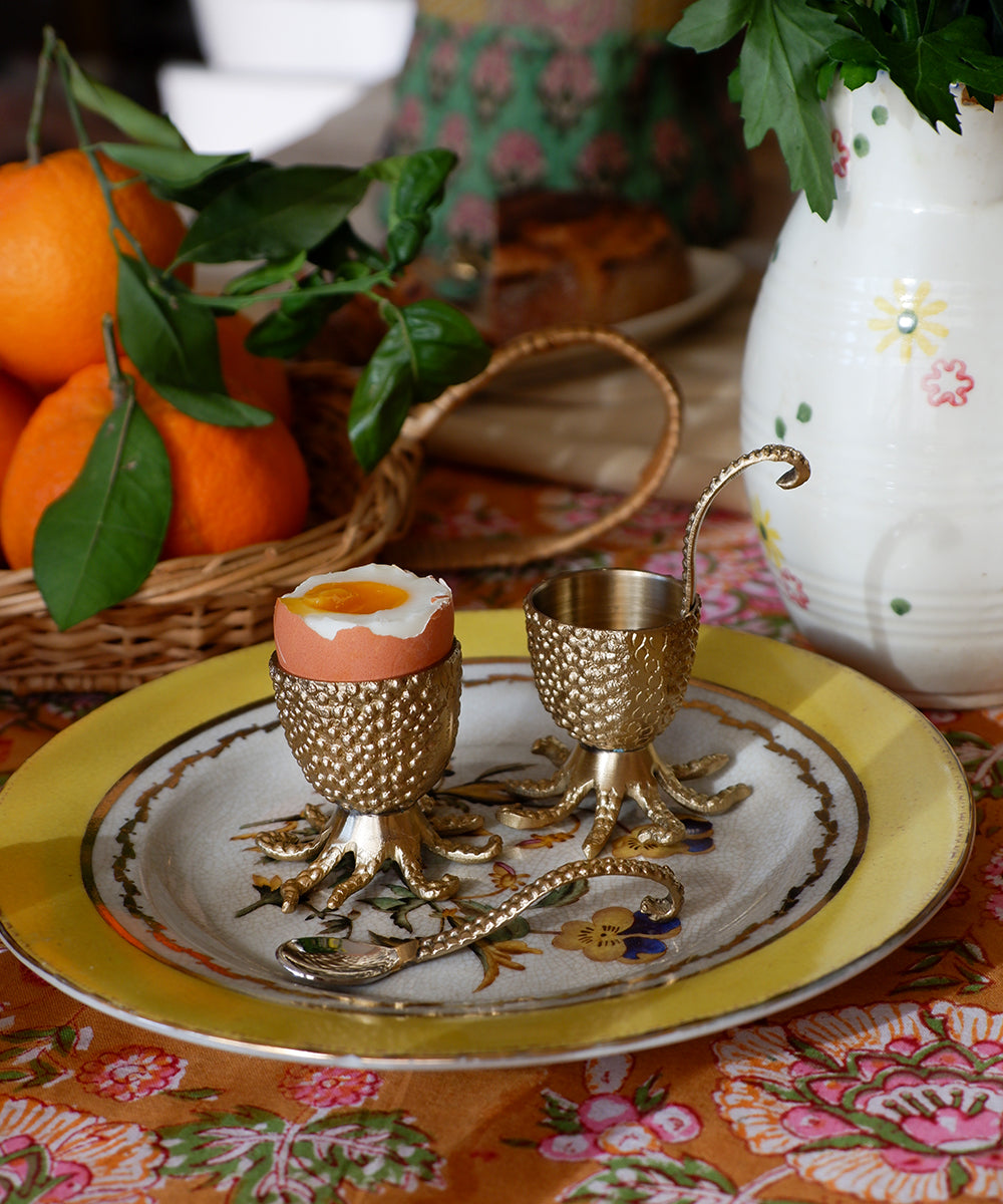 Eggeholder i messing på en tallerken på et bord med en mønstrete duk