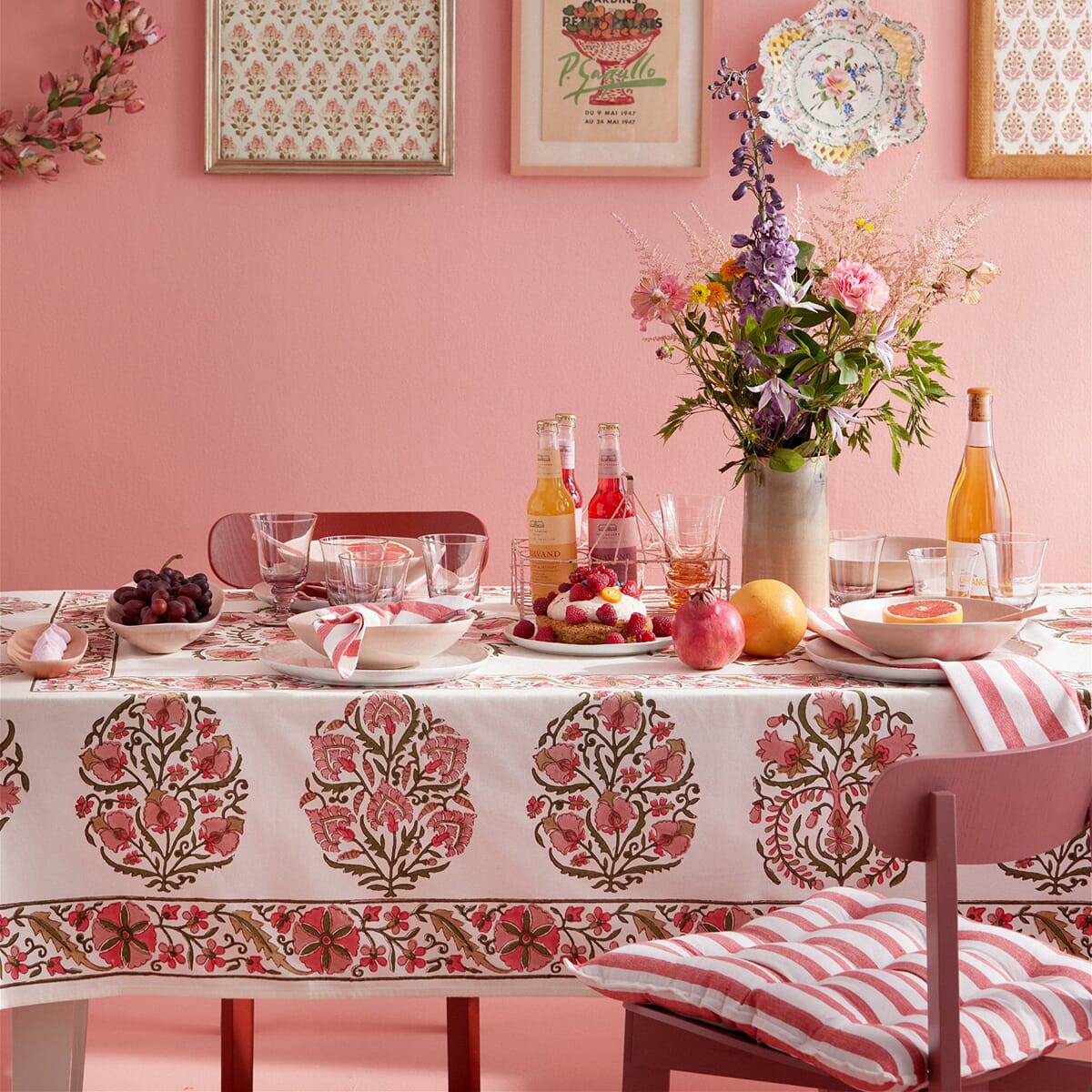 Dekket bord med mønstret duk i rosa og grønt, glass, servise og friske blomster, stylet i et rom med rosa vegger.