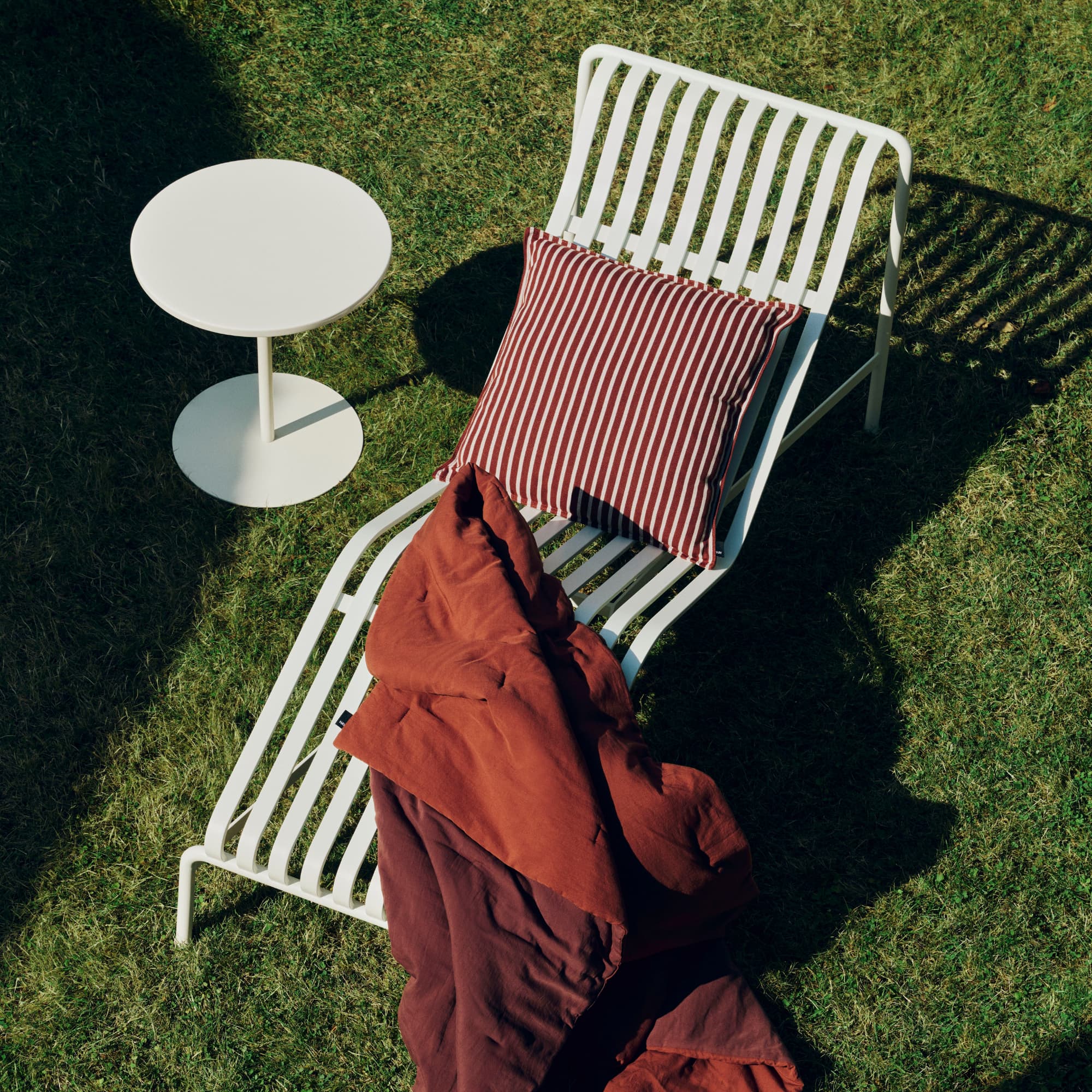 Utepute med røde og hvite striper sammen med rødt pledd i en lungesolseng på gresset