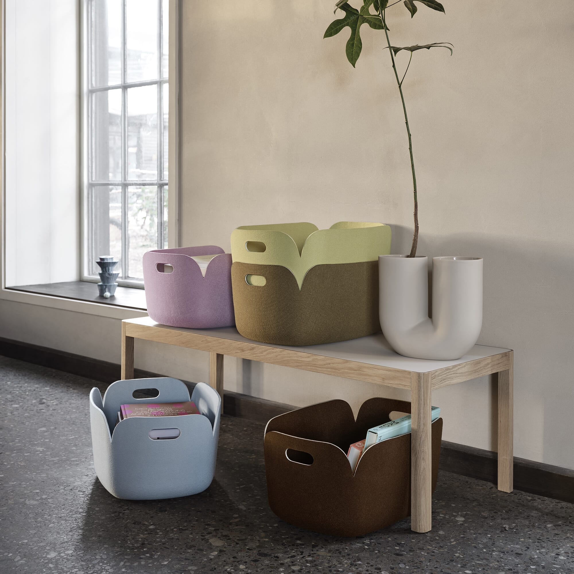 Restore basket fra Muuto, kurver i forskjellige farger plassert på en benk og på et terrazzo gulv.