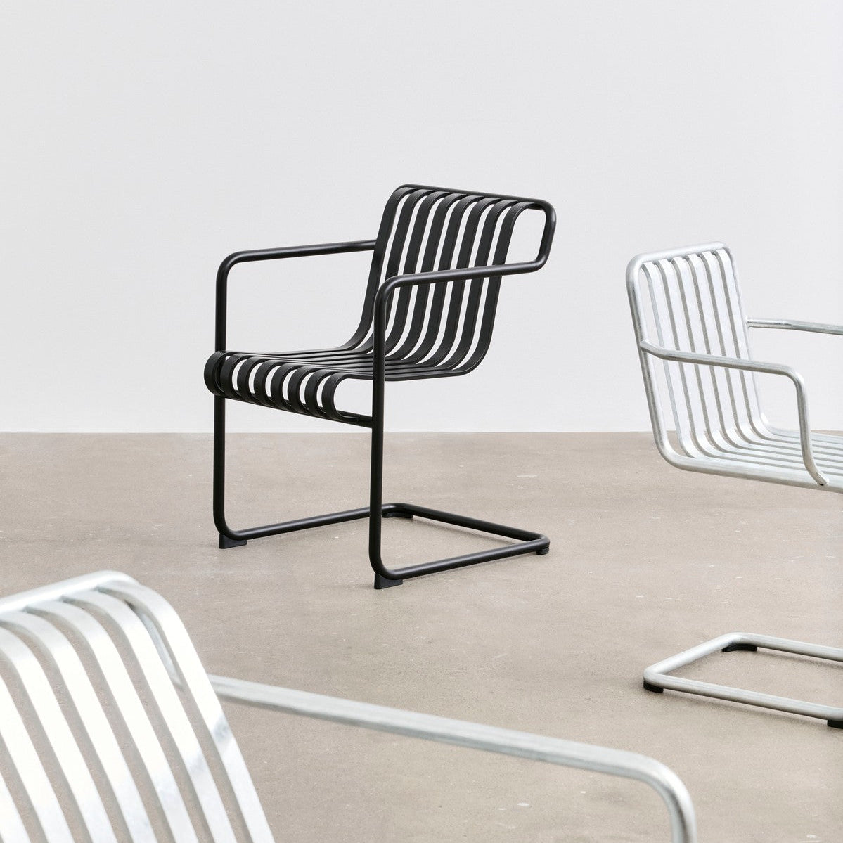 Plissade spisestol Cantilever med armlene i svart på betonggulv