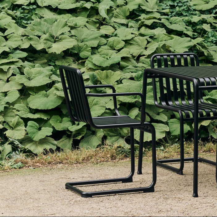 Plissade spisestol Cantilever med armlene i svart på uteplass med grus