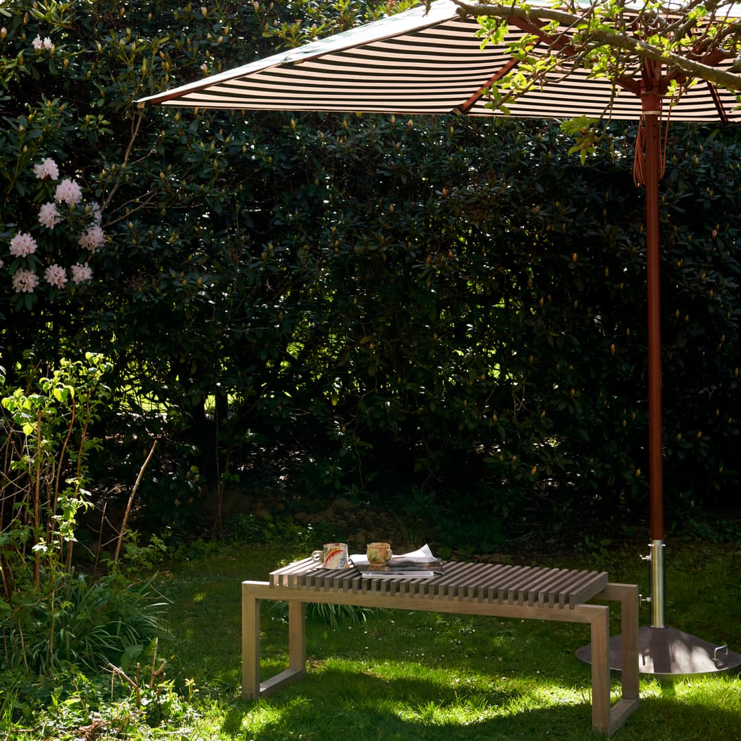 Cutter benk i teak i hagen på gresset under en Messina parasoll.