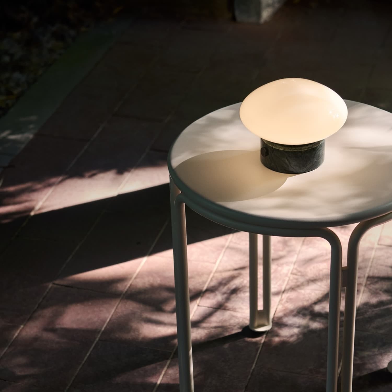 Oppladbar Mist bordlampe i glass og marmor verde plassert på ett sidebord ute