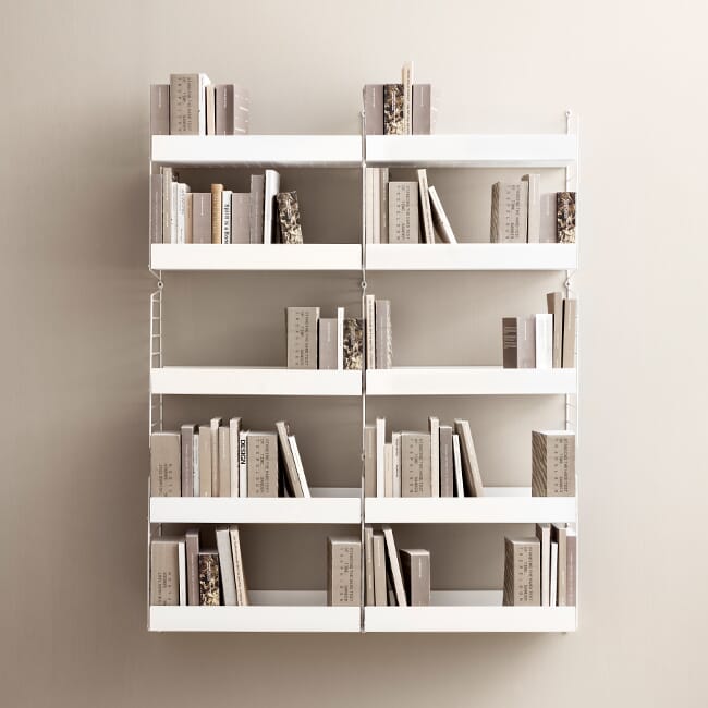 To stykk String veggreol 60 × 150 med perforerte hyller ved siden av hverandre med bøker i stue