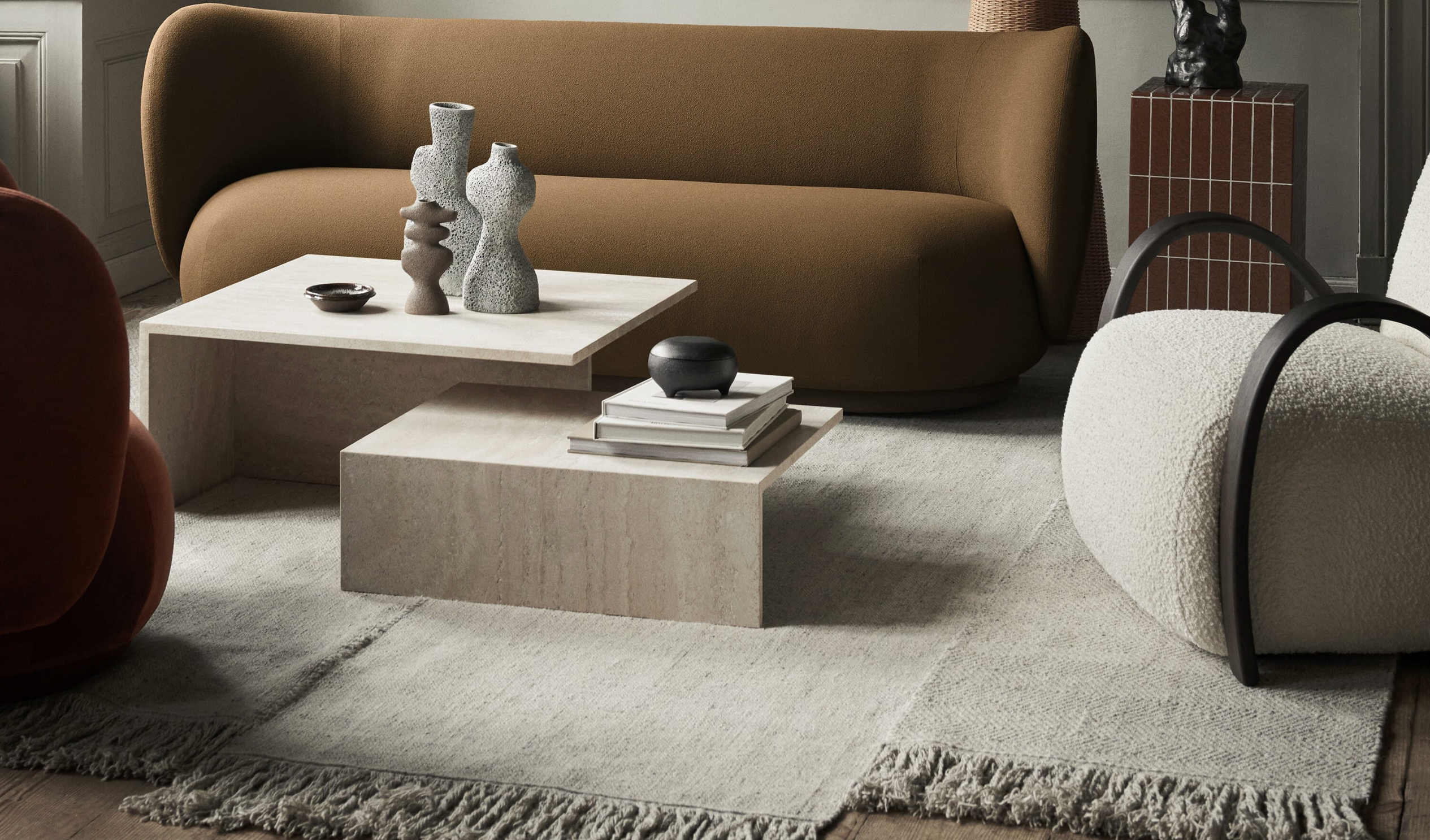 Moderne stue med stein sofabord, brun sofa og hvit loungestol på et lyst, frynset teppe.