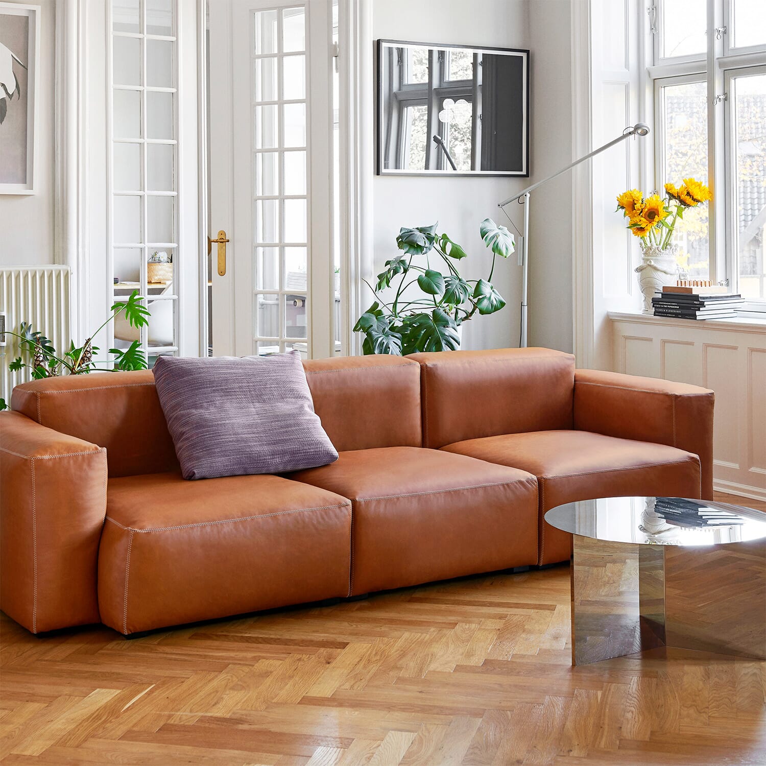Lyst spiseområde med rund spisebord og polstrede stoler i duse toner, dekorert med vase, bøker og moderne interiør ved store vinduer.