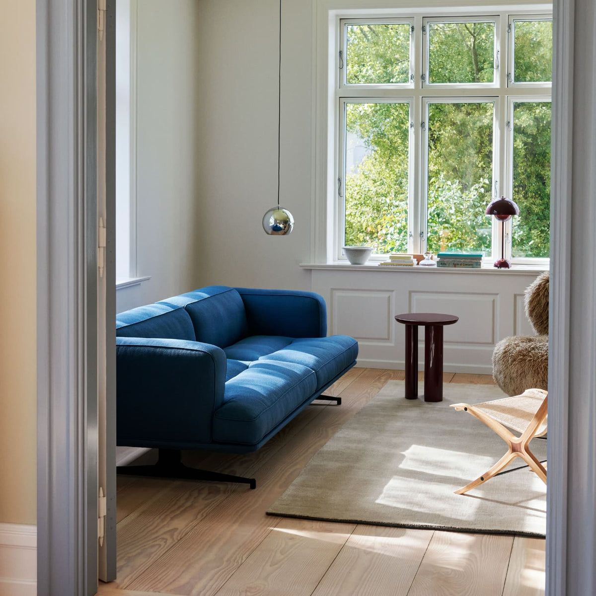 Sofa Inland fra &Tradition i blå farge i en beige klassisk stue, med brede planker tregulv og et beige teppe. Bordlampen Flowerpot i vinduskarmen