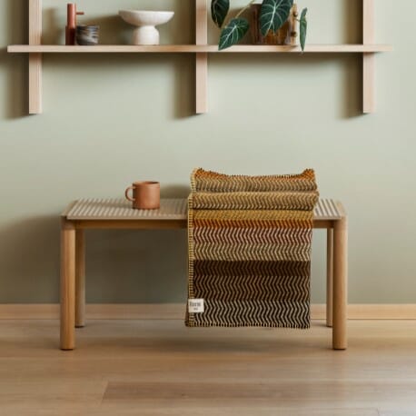 Ullpledd i varme farger plassert på en benk.