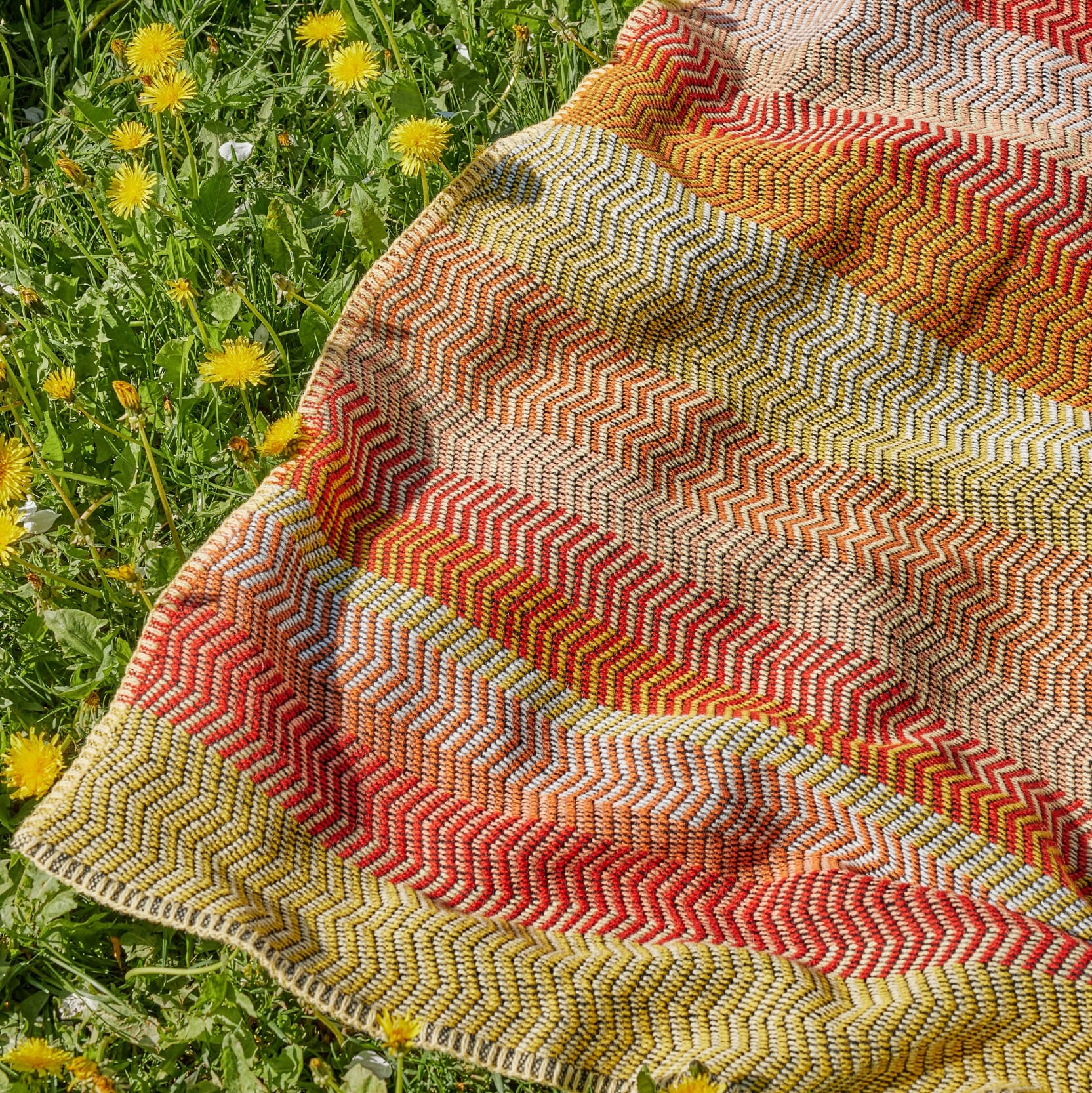 Ullpledd Fri Summer Red med myk sikksakk og varme fargetoner, lagt utendørs på gress for å vise naturlig bruk.