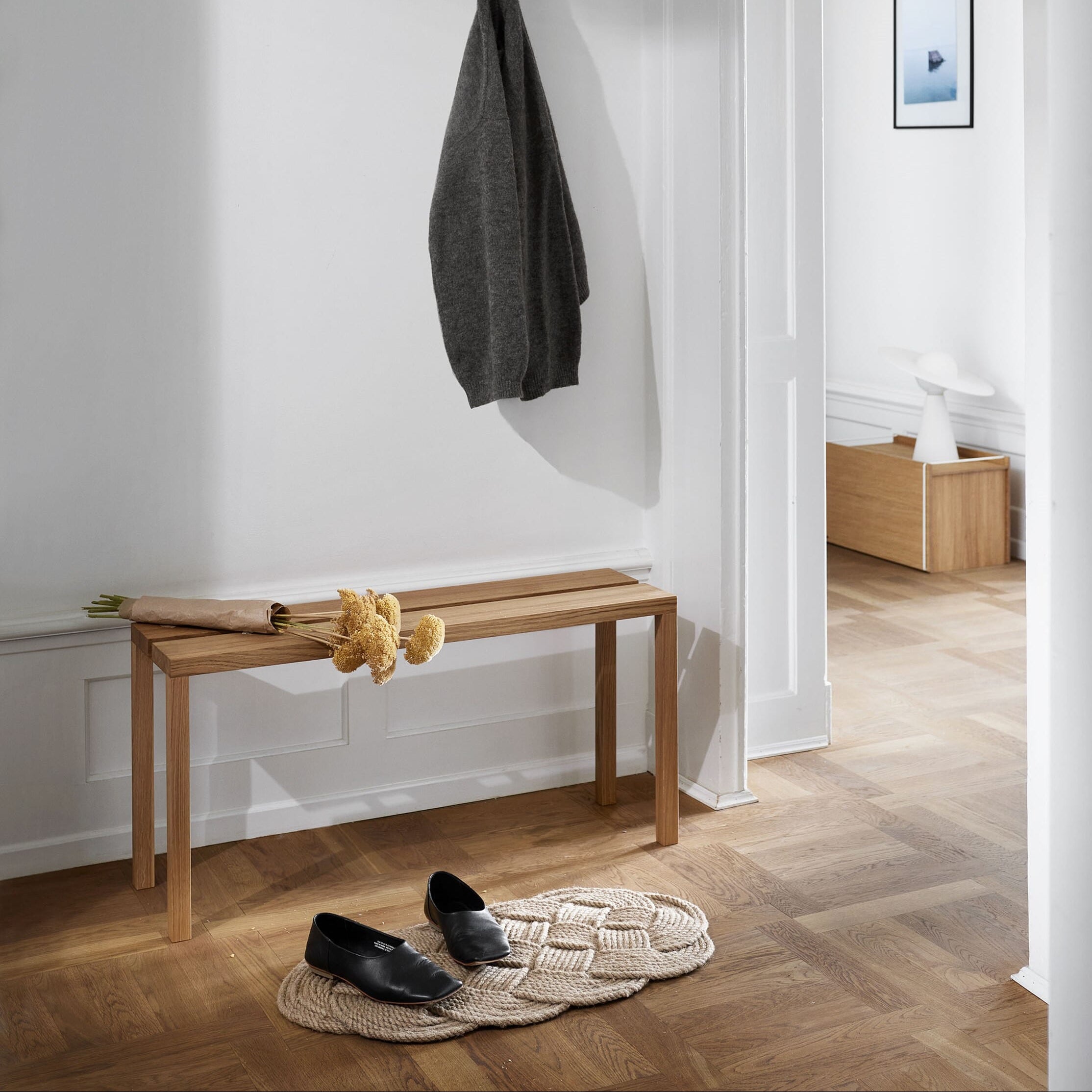 Smal benk i eik plassert i gang, brukt som sitteplass og avlastning i et lyst og ryddig interiør.