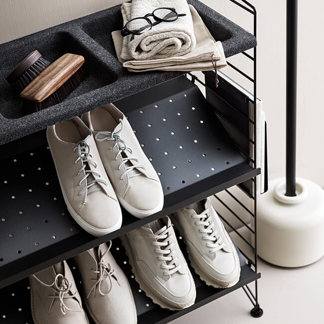 String skohylle i svart med to hylleplater i metall og en skålhylle vist med sko